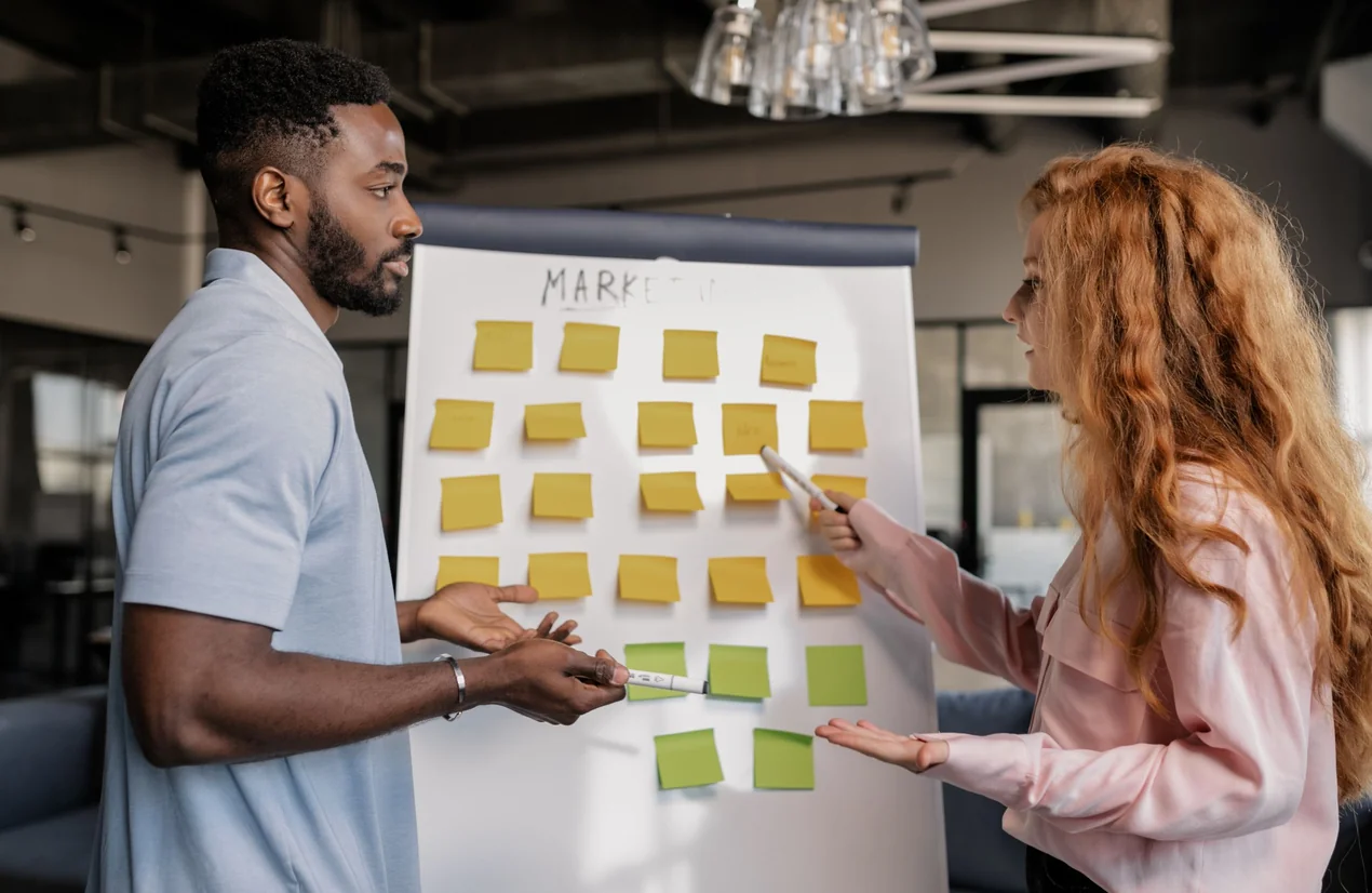 Dos personas organizando ideas con notas adhesivas en un tablero de marketing