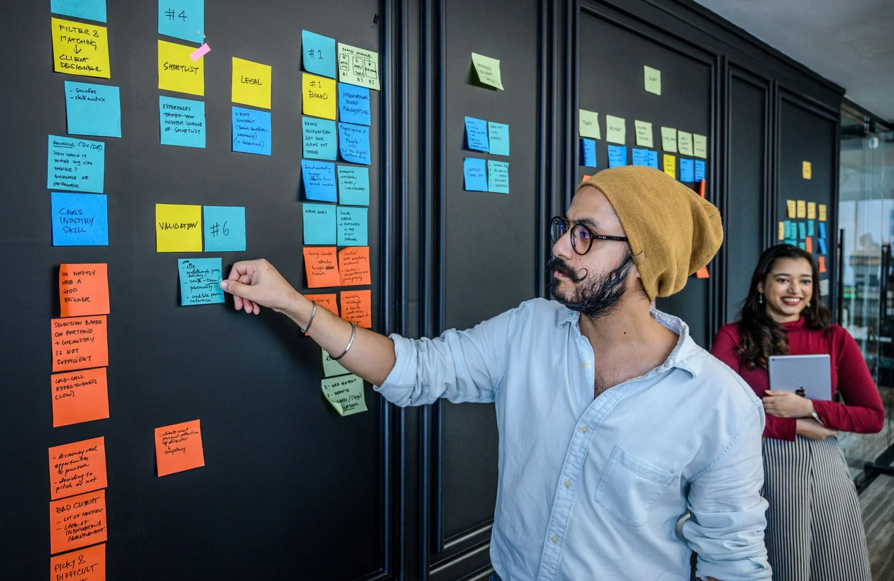 Un compañero ordenando tareas en una pared de notas adhesivas de colores